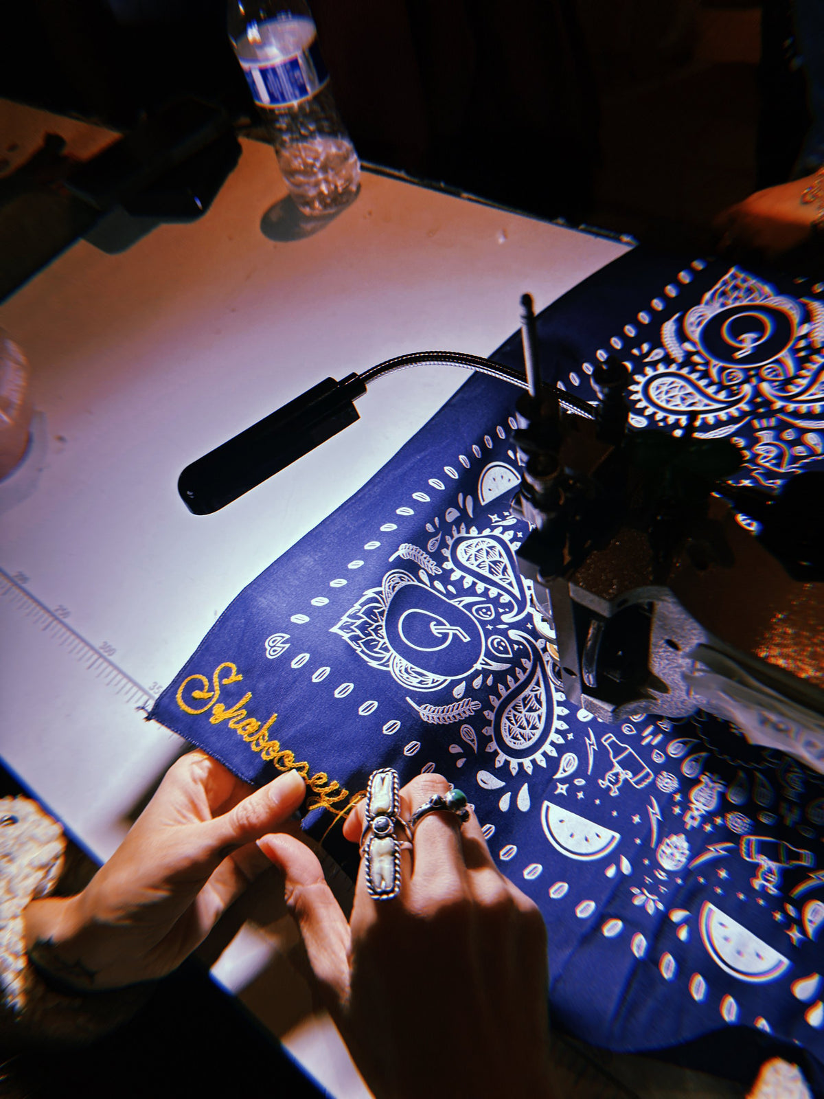 Hands guiding a bandana under the chainstitch machine